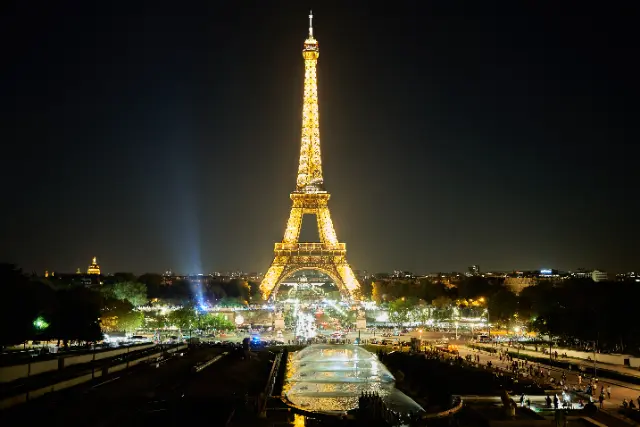 The illuminated Eiffel Tower stands tall against a dark night sky overlooking the city of Paris.